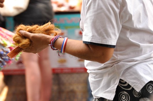 Khao San Road, Bangkok, Thailand. There are many stands and stalls all along Khao San where tourists can get braids and extensions and other funky things done to their hair.  This lady was just walking around with a handful of fake hair and comb. 